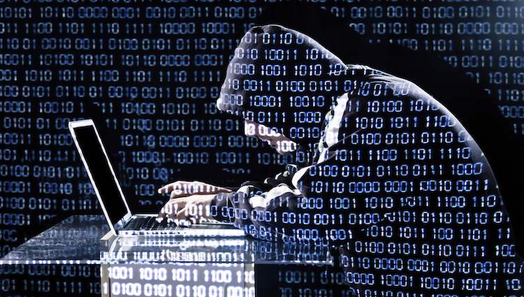 Man wearing a hooded sweatshirt hacking a laptop with blue binary numbers overlapping everything in the photo
